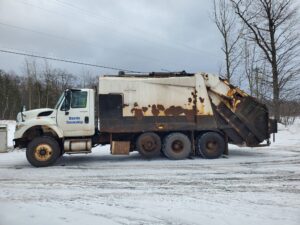 Rusty garbage truck in snowy landscape.